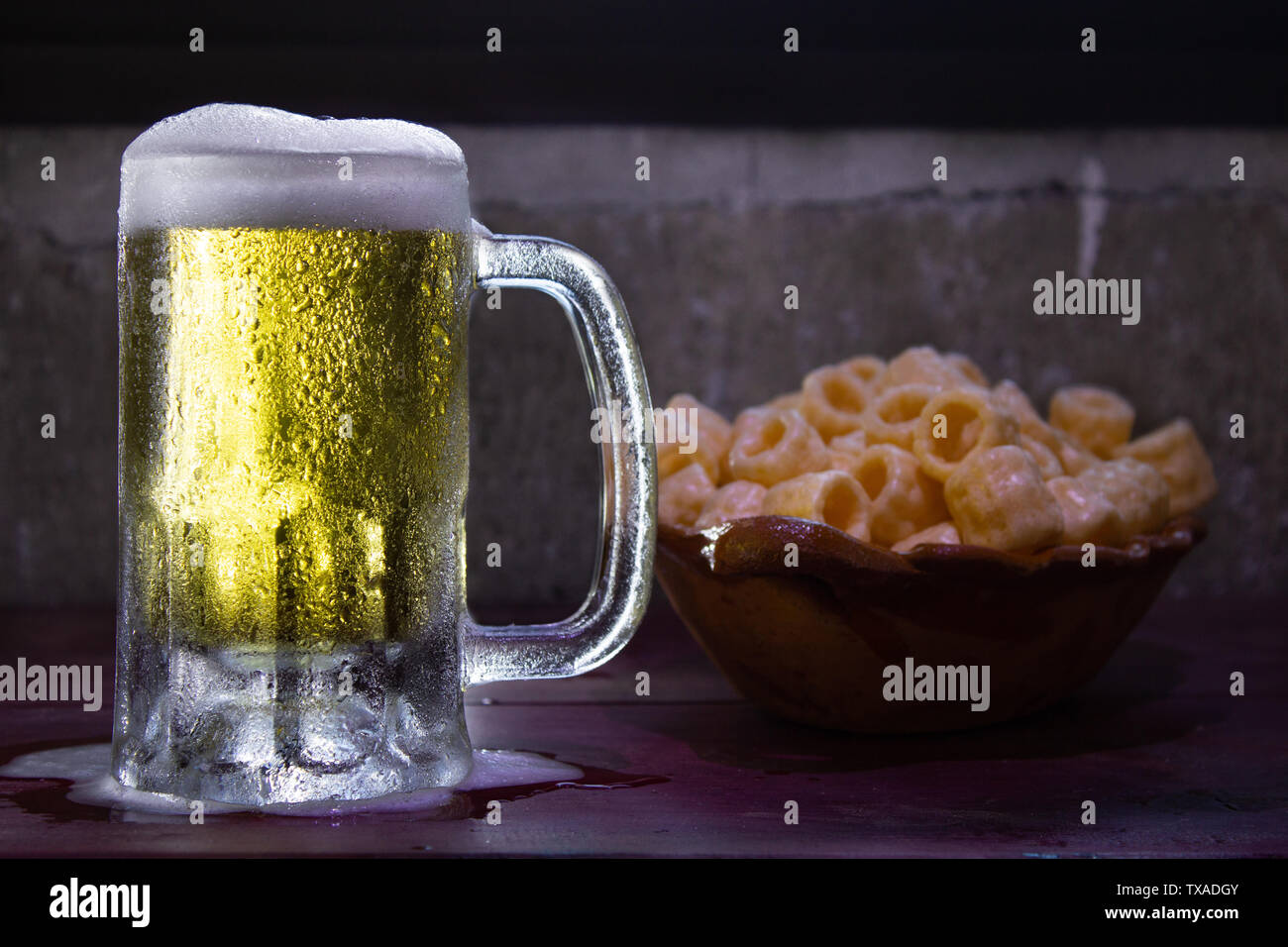 a frozen beer mug with foam pouring on a red wood table with fried snacks Stock Photo