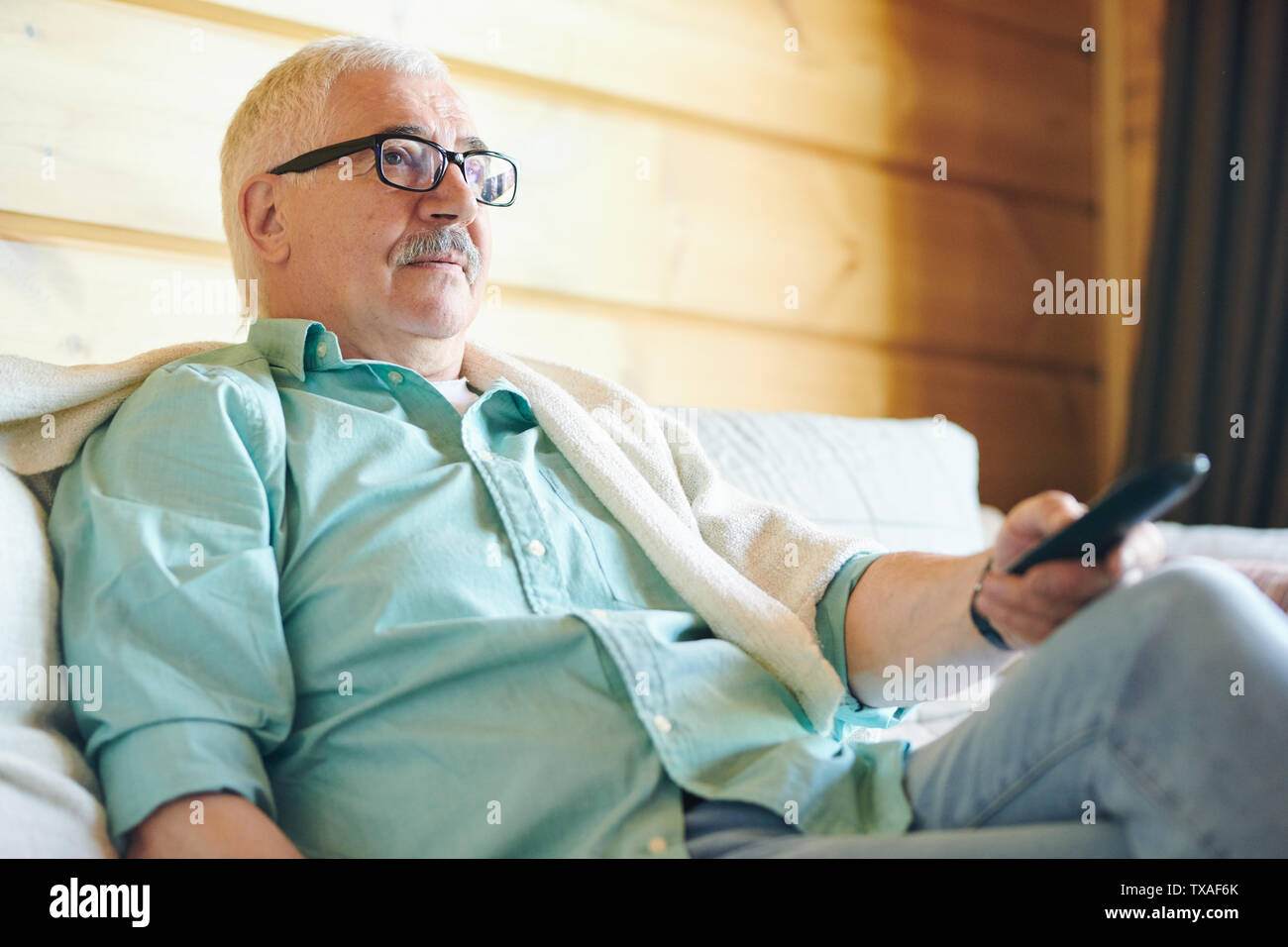 Restful senior man in eyeglasses and casualwear using remote control Stock Photo