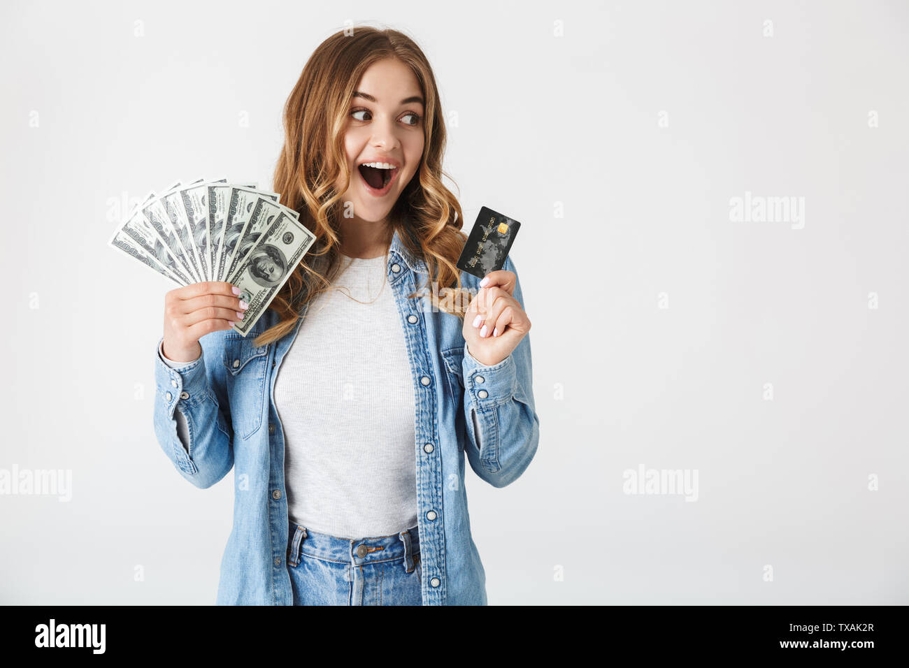 Attractive excited young girl standing isolated over white background, showing money banknotes and credit card Stock Photo