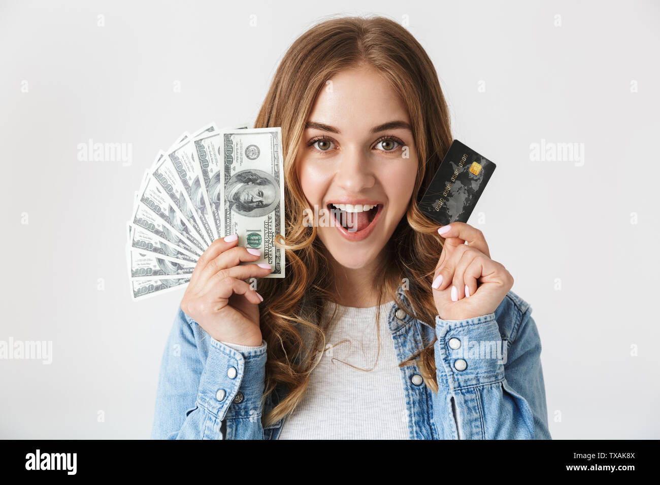 Attractive excited young girl standing isolated over white background, showing money banknotes and credit card Stock Photo