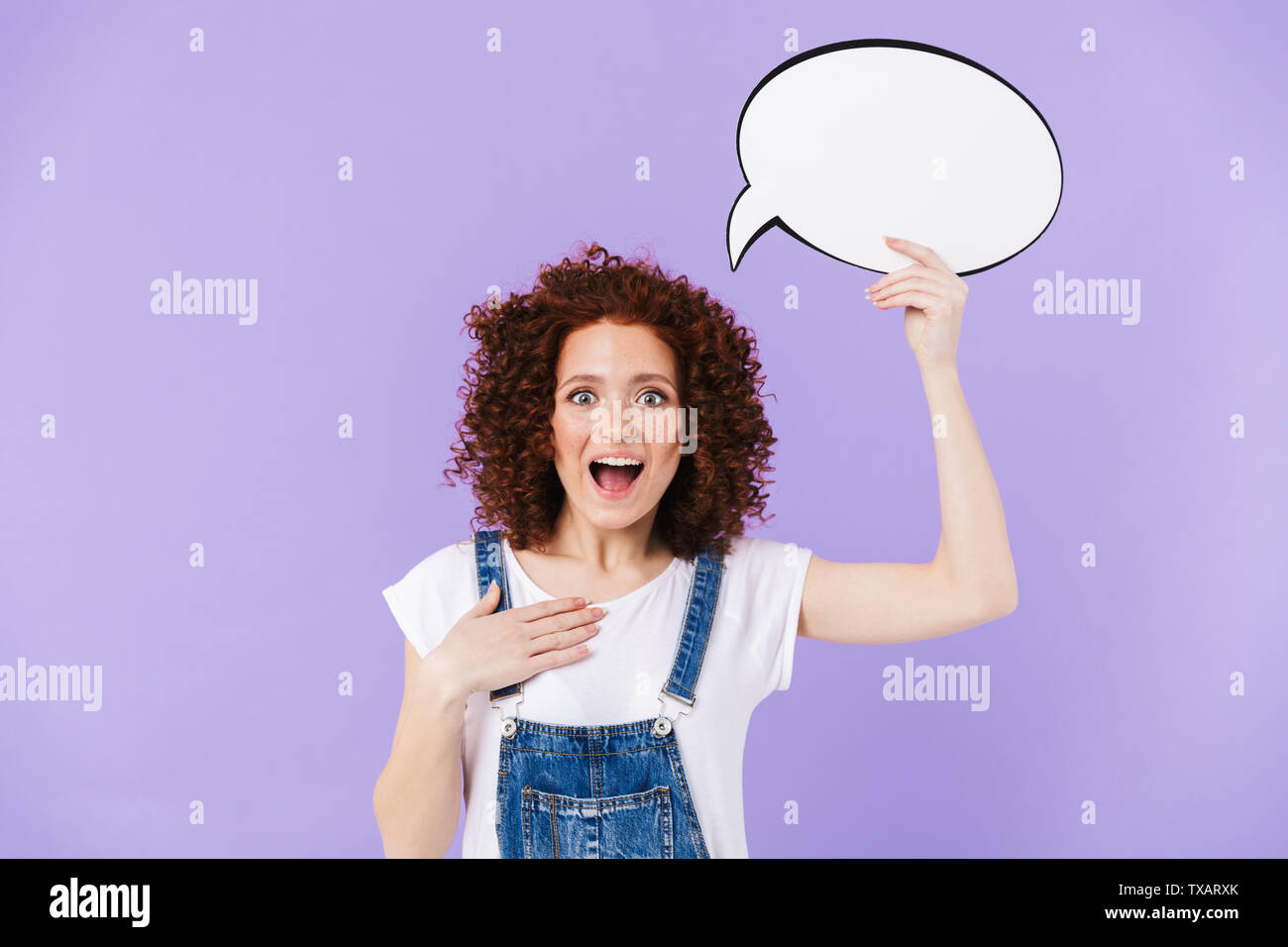 Portrait of pleased redhead curly woman 20s smiling while holding blank thought bubble Stock Photo