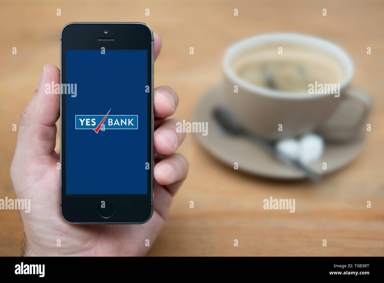 A man looks at his iPhone which displays the Yes Bank logo (Editorial use only). Stock Photo