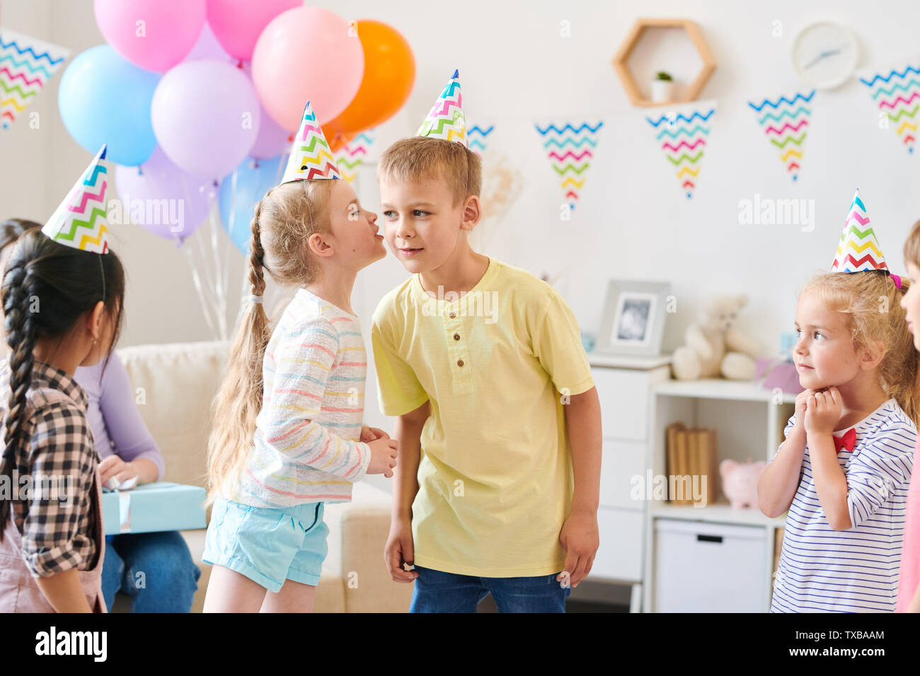 Cute little girl in casualwear whispering something to boy while playing game Stock Photo