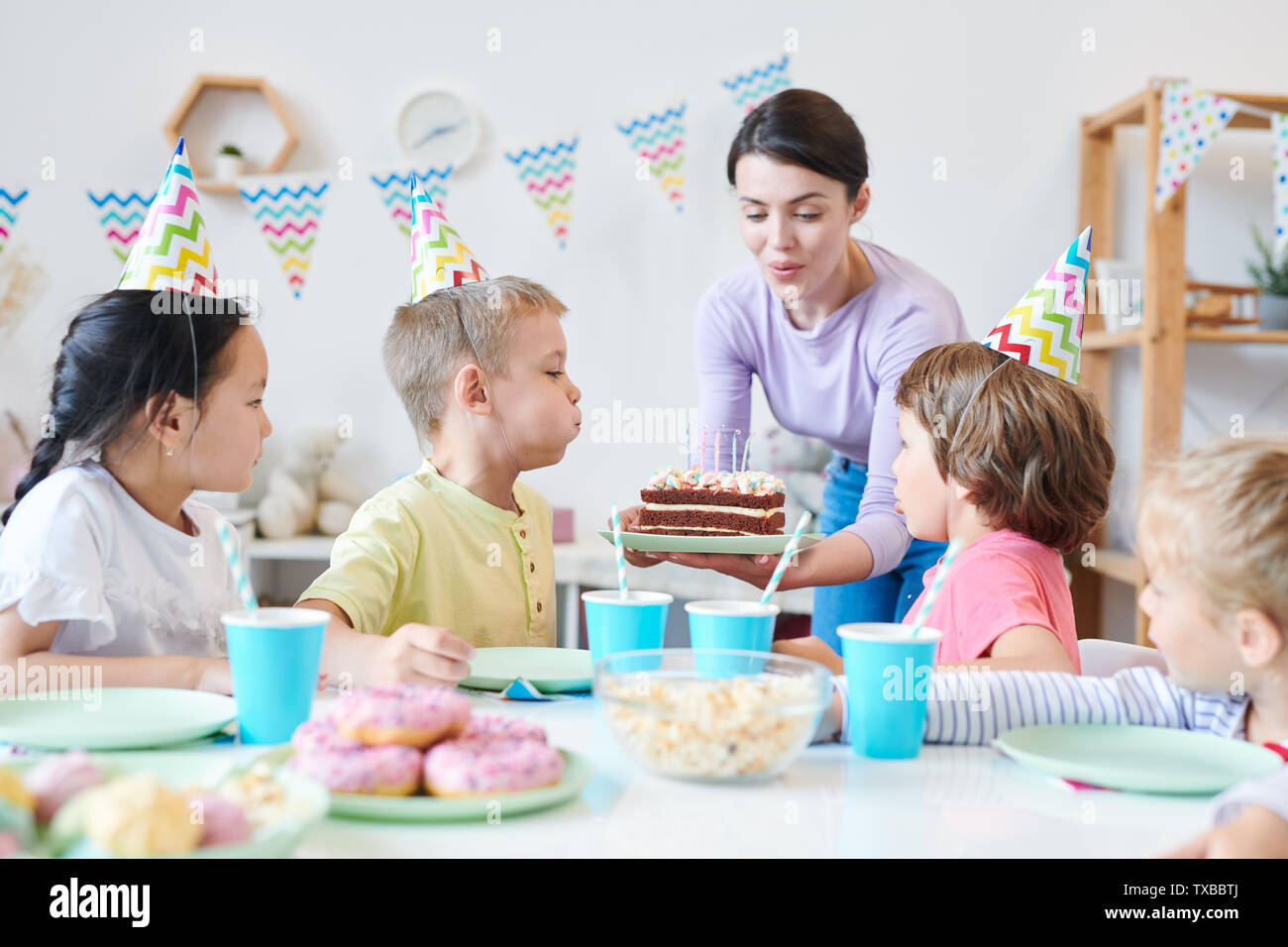 Young mother helping little kids to blow candles on birthday cake Stock