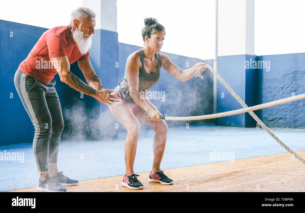 Fit woman training with battle rope inside gym - Hipster personal trainer motivating a female athlete who's doing endurance exercises Stock Photo