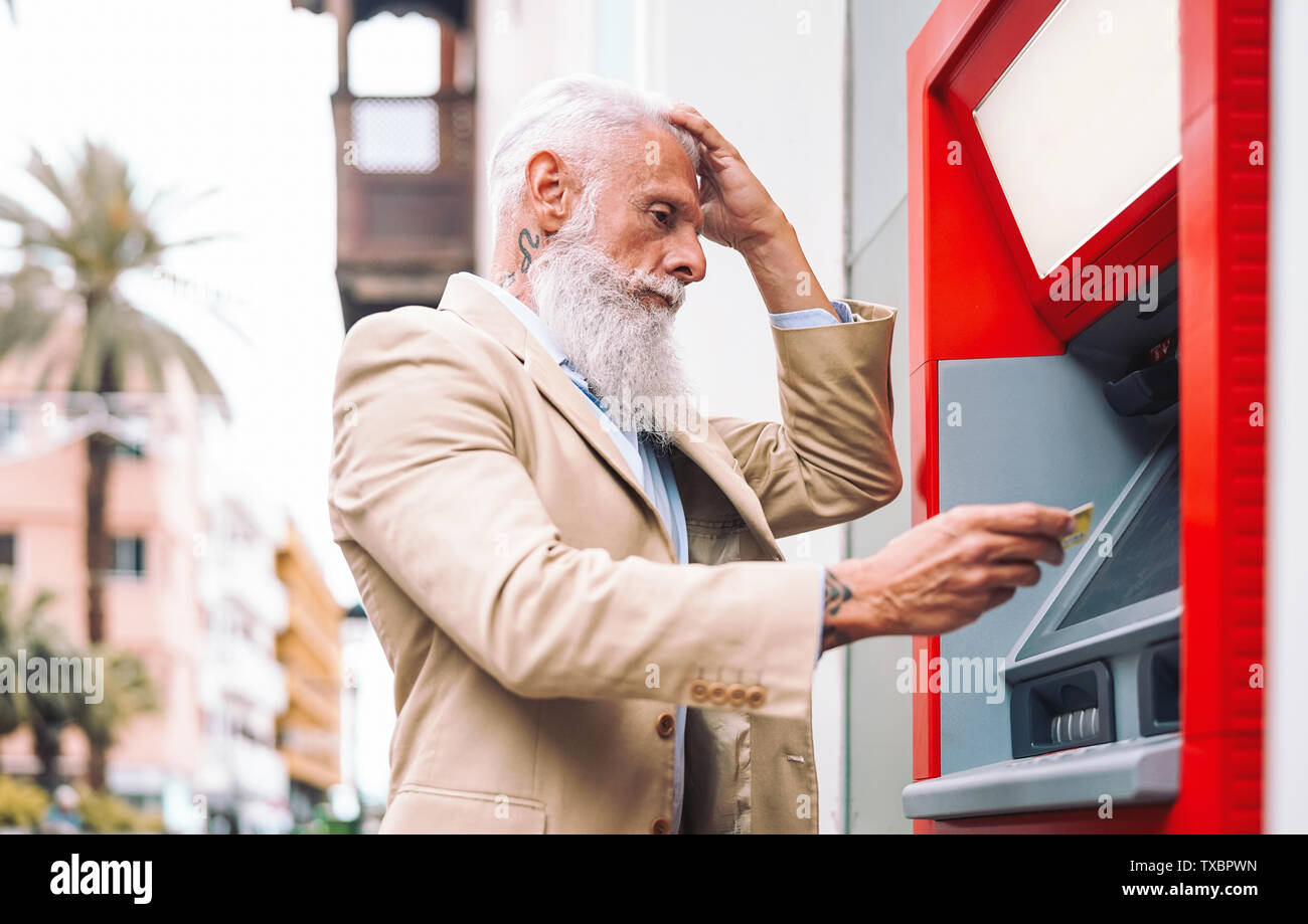 Happy mature man withdraw money from bank cash machine with debit card - Senior male doing payment with credit card in ATM Stock Photo