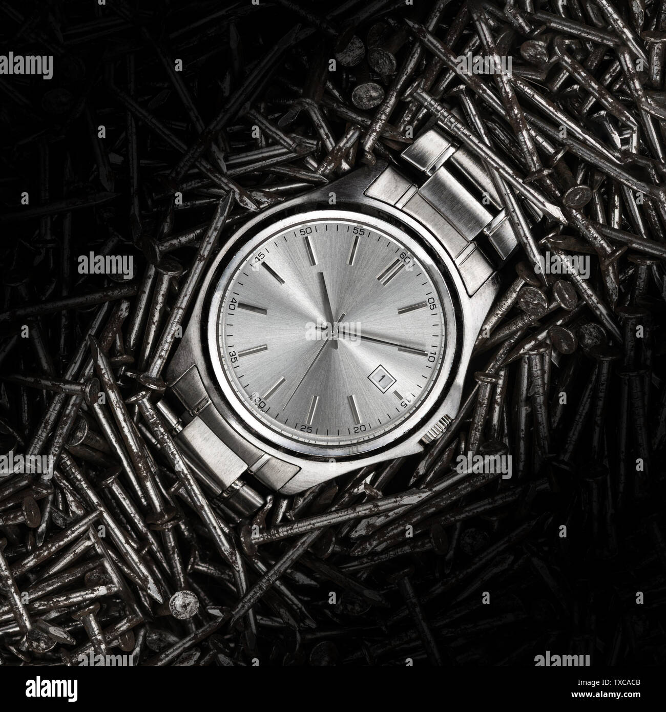 A beautiful stainless steel metal wrist watch laying on a bed of metail construction nails closeup macro Stock Photo