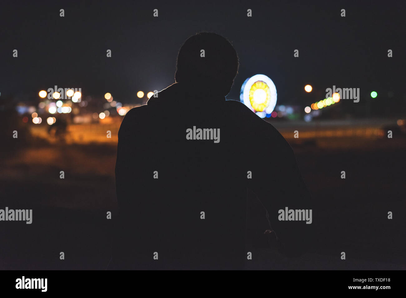 Silhouette of a man leaning on a highway overpass barrier at night. He ...