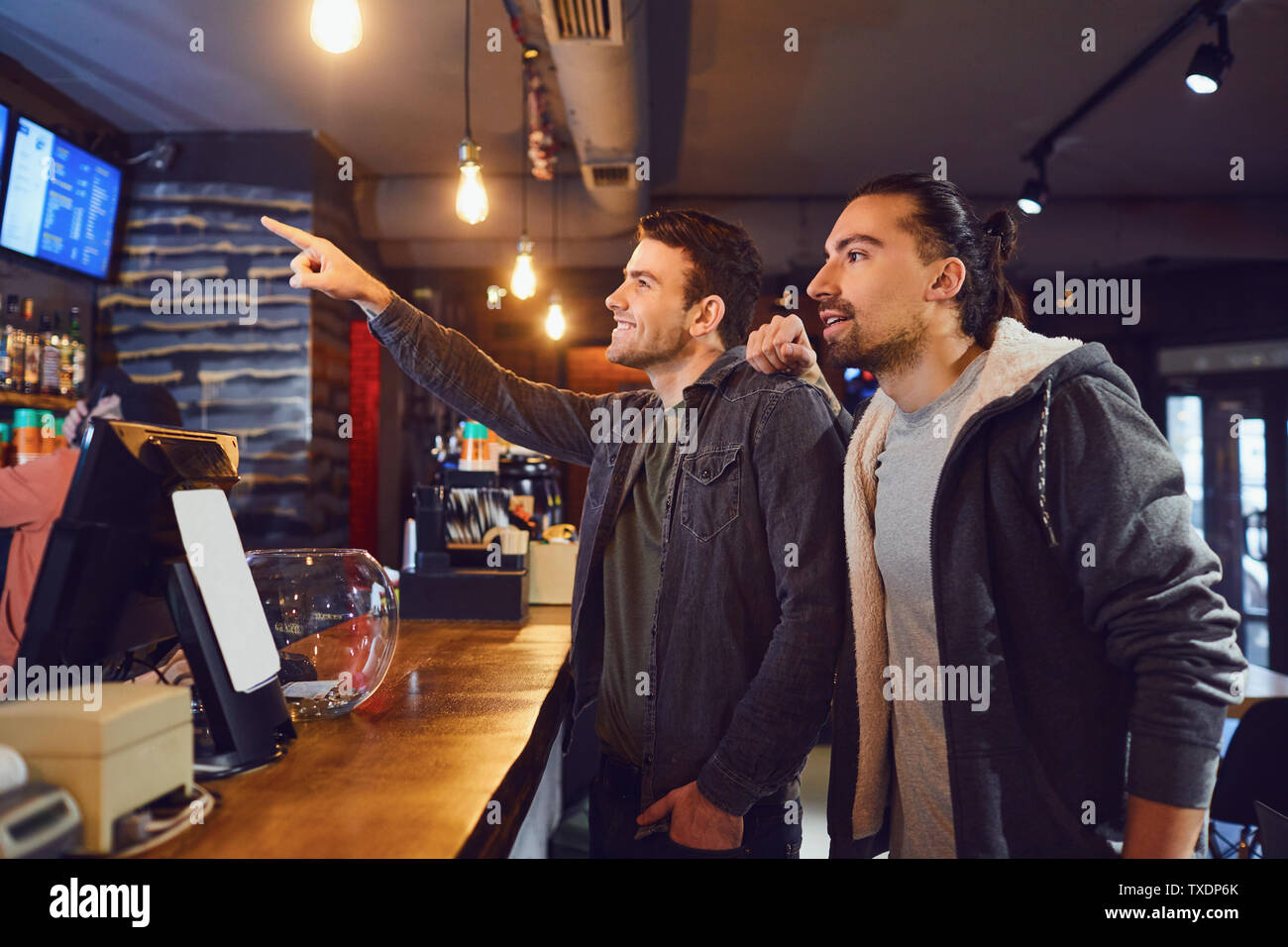 Side view of two young men reading menu and choosing beverage while standing near counter in modern pub Stock Photo