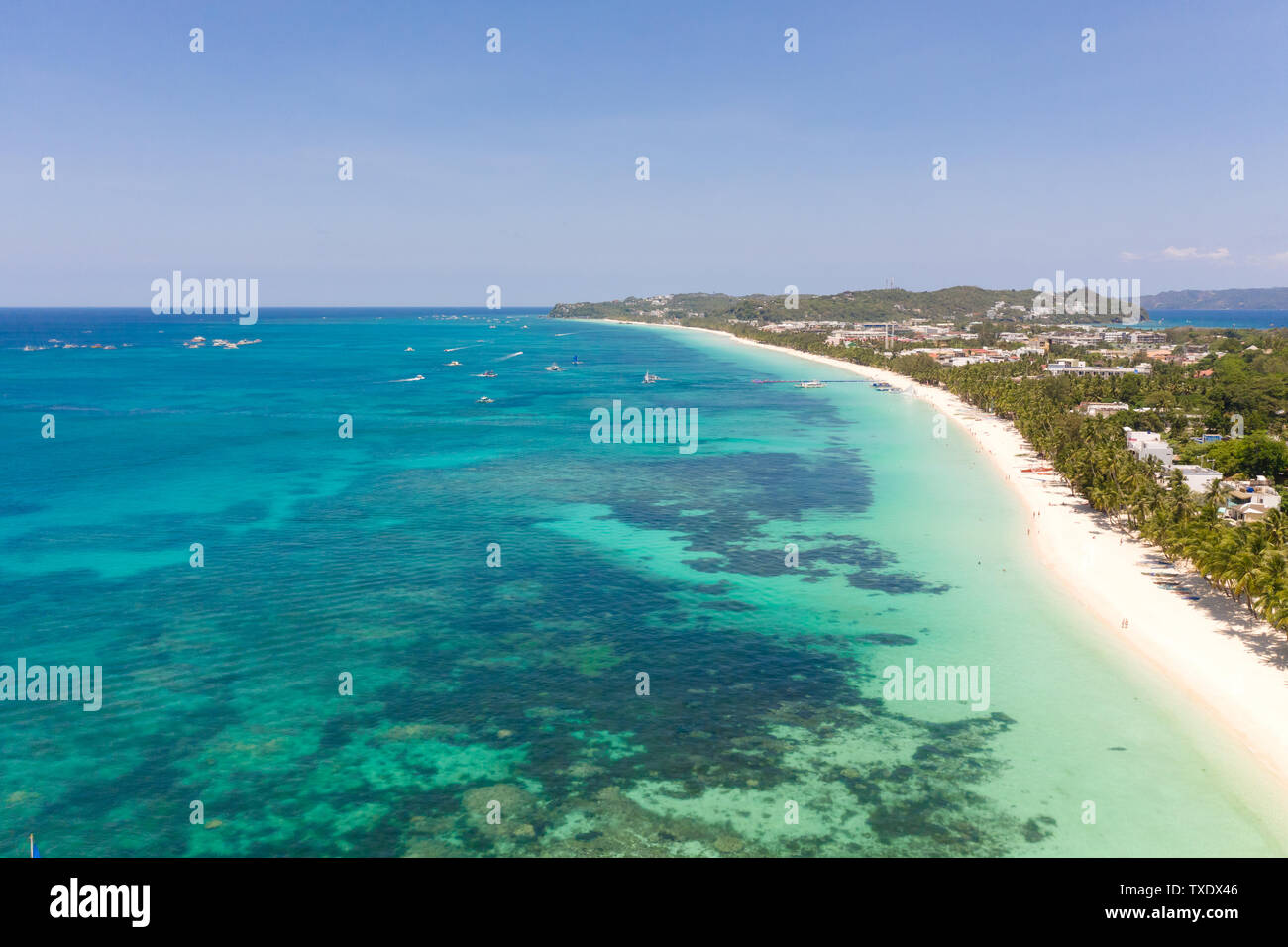 Seascape in the Philippines in sunny weather, view from above. Transparent sea and tourist boats near the island of Boracay. Residential buildings and hotels on the big island. Stock Photo