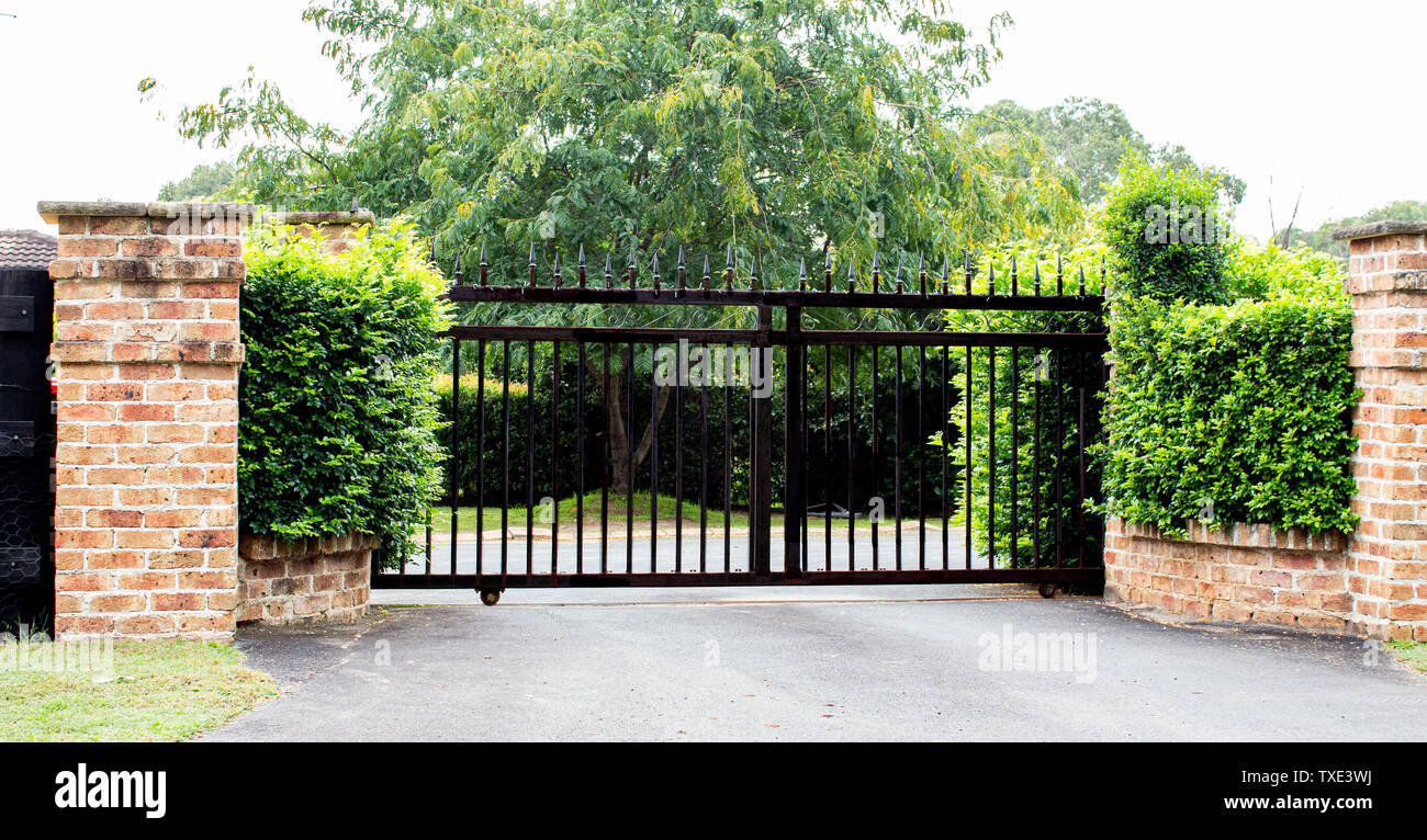 Black metal driveway property entrance gates set in brick fence with