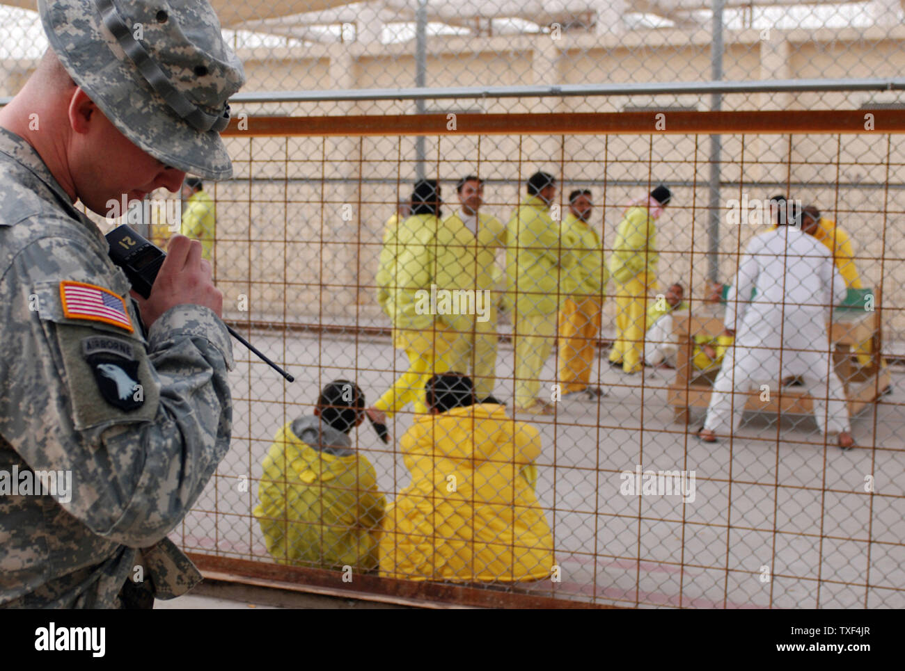 Army Staff Sgt. Gregory Smith, 535th Military Police Battalion, monitors his radio on one of his many daily patrols inside Compound 2 at Camp Cropper, a Theater Internment Facility (TIF) in western Baghdad, Iraq on June 1, 2008. Behind him, detainees play a game of table tennis in the recreation yard. (UPI Photo/Spc. Michael V. May/Army) Stock Photo