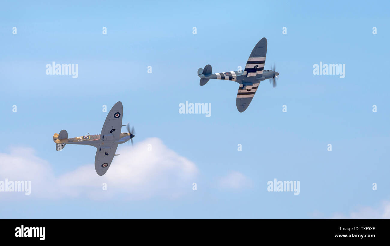 Weston-super-Mare, UK. 22nd June, 2019. Battle of Britain memorial flight with two spectacular, vintage spitfire aircraft flying high in a blue, summer sky through wispy, light clouds, together at the Weston Air Festival 2019 over the coastline of Weston-super-Mare. Credit: Lee Hudson Stock Photo