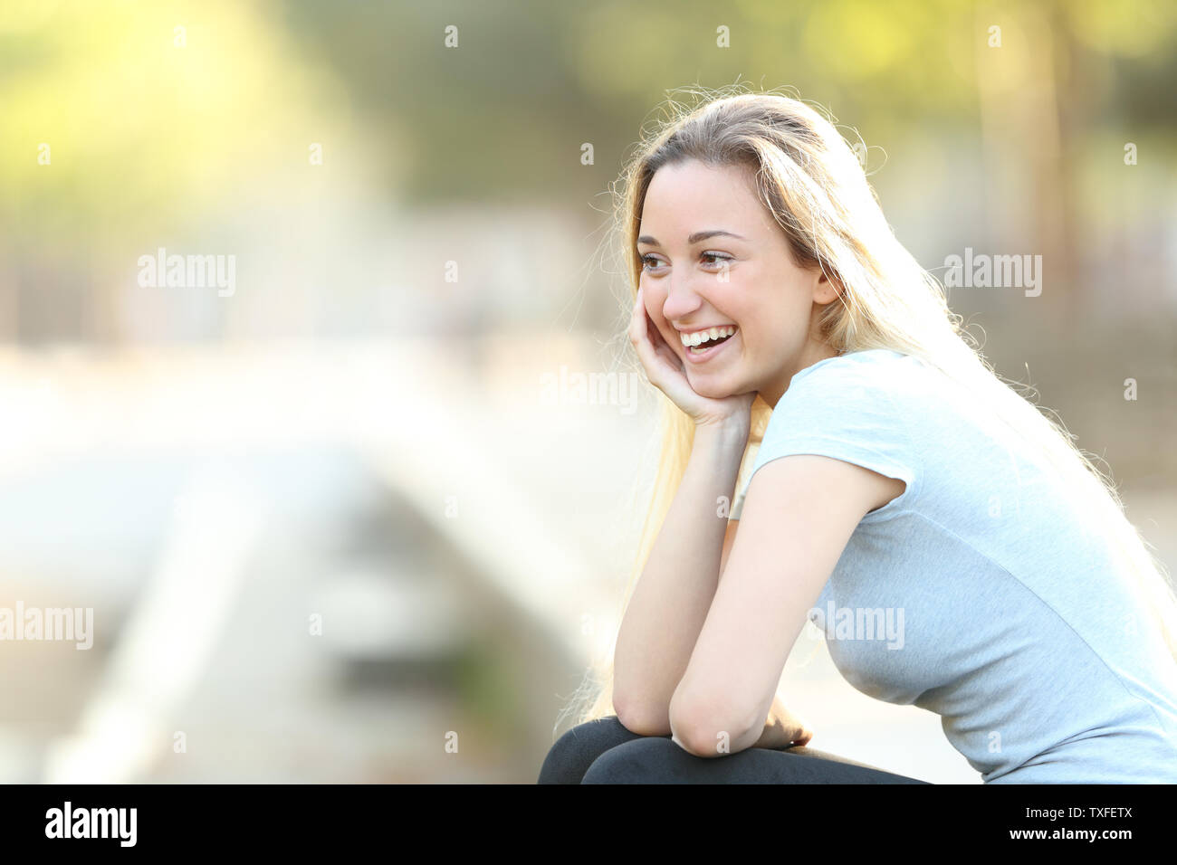 Happy teenage girl laughing looking away sitting in a park with copy space Stock Photo