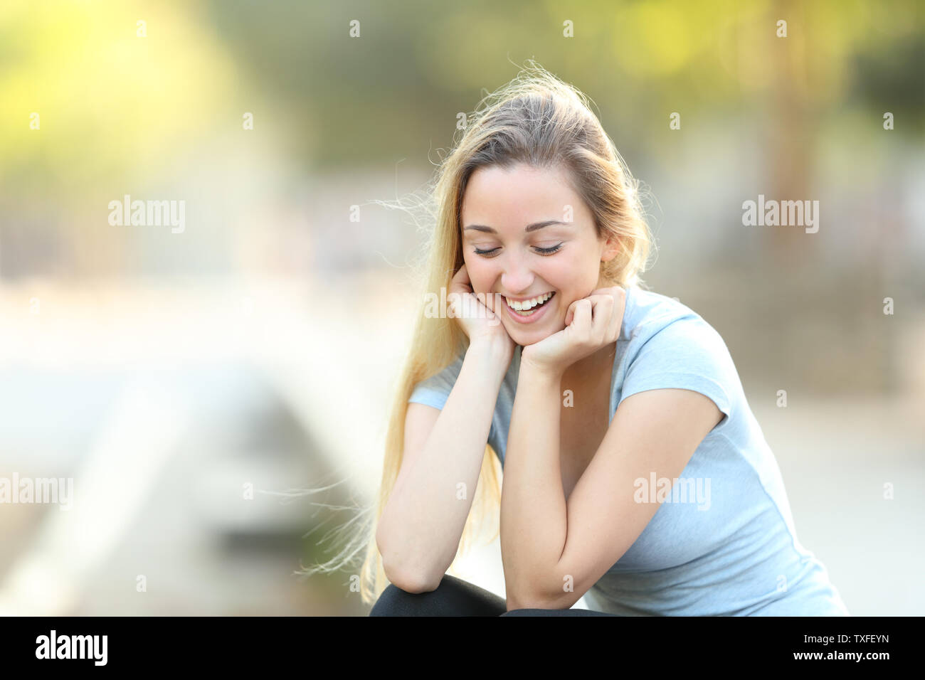 Candid teenage girl laughing looking down sititng in a park Stock Photo