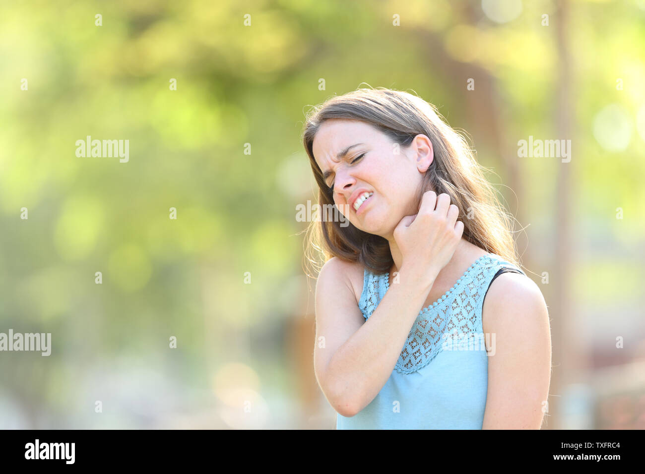 Woman suffering itching scratching neck standing outdoors in a park Stock Photo