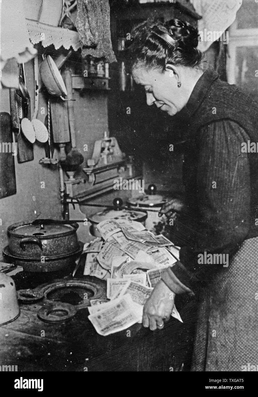 Inflation. In Germany after the last war, it was possible to pay 50 million dollars for a nickel cup of coffee, and 35 million dollars for a $35 suit of clothes. This Berlin woman, realizing that fuel costs money, is starting the morning fire with marks not worth the paper they are printed on Stock Photo