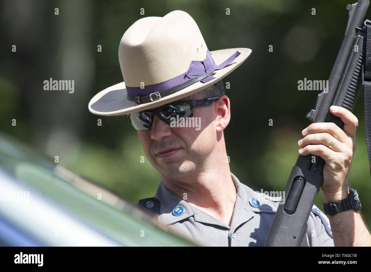 A law enforcement officer with a shotgun stands at the scene along
