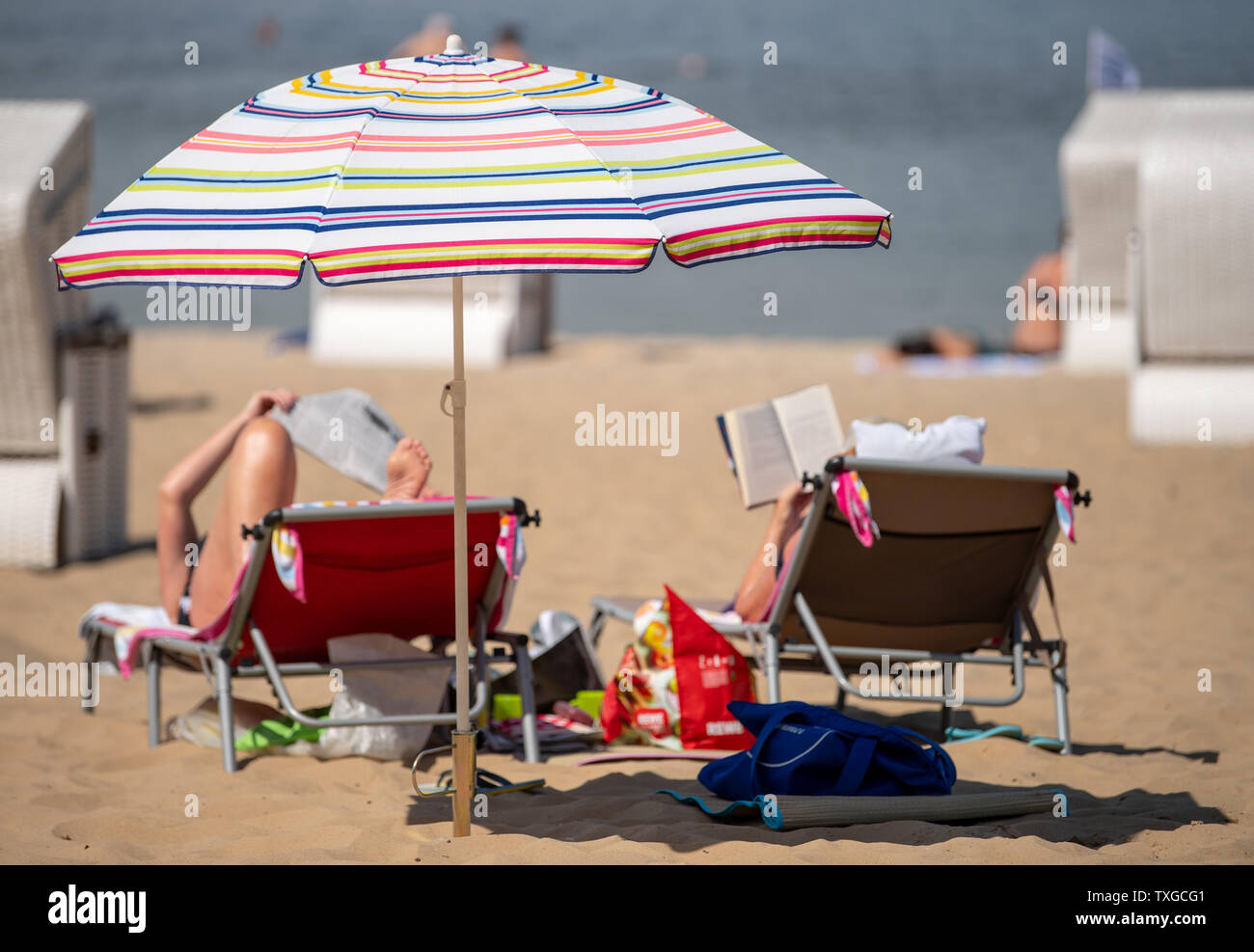 25 June 2019, Berlin: Two women enjoy the summer weather on deck chairs under a parasol at the Wannsee lido. This week temperatures well above 30 degrees Celsius are expected in Berlin. Photo: Monika Skolimowska/dpa-Zentralbild/dpa Stock Photo