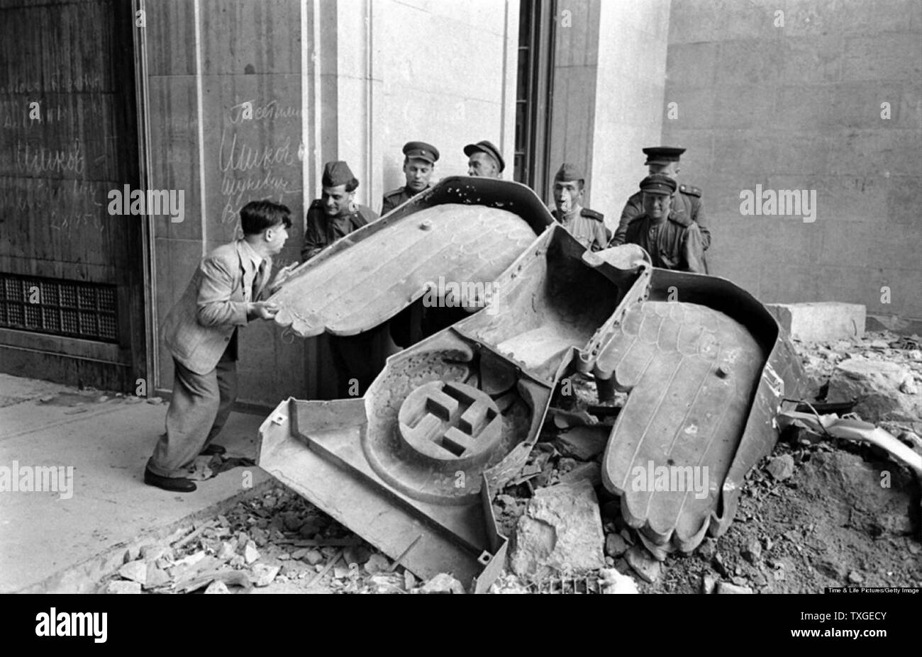 Photograph of Russian soldiers and a civilian struggle to move a large bronze Nazi Party eagle that once loomed over a doorway of the Reich Chancellery, Berlin. Dated 1945 Stock Photo