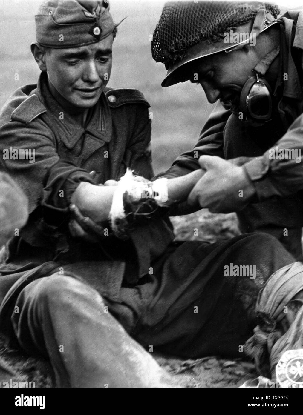 A captured, teenage, German soldier cries as he is treated for his wounds by an American soldier as they wait for a medic to arrive. From Cherbourg, France. Stock Photo