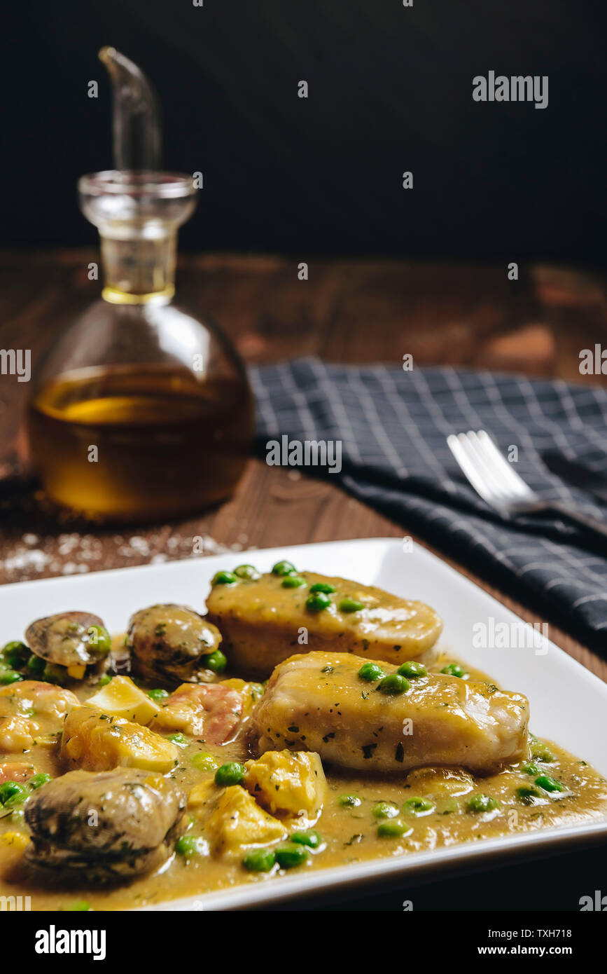 vertical photo of healthy traditional spanish hake dish with green seafood sauce with clams