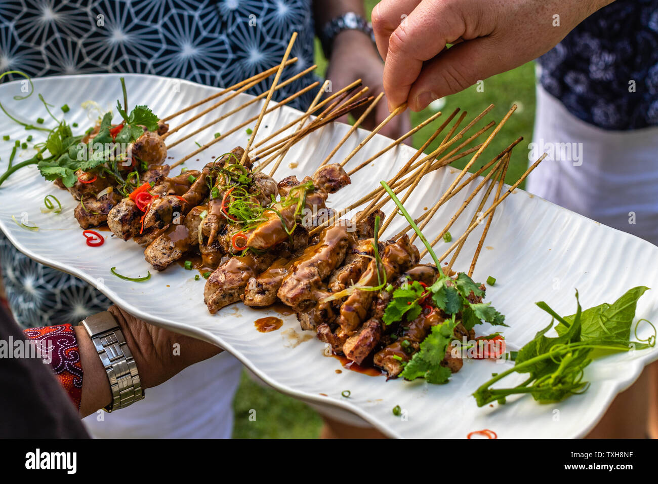 Sate ayam, grilled chicken meat on wooden skewers served with sambal kacang, peanut sauce. Hands taking the skewers. Indonesian cuisine. Stock Photo