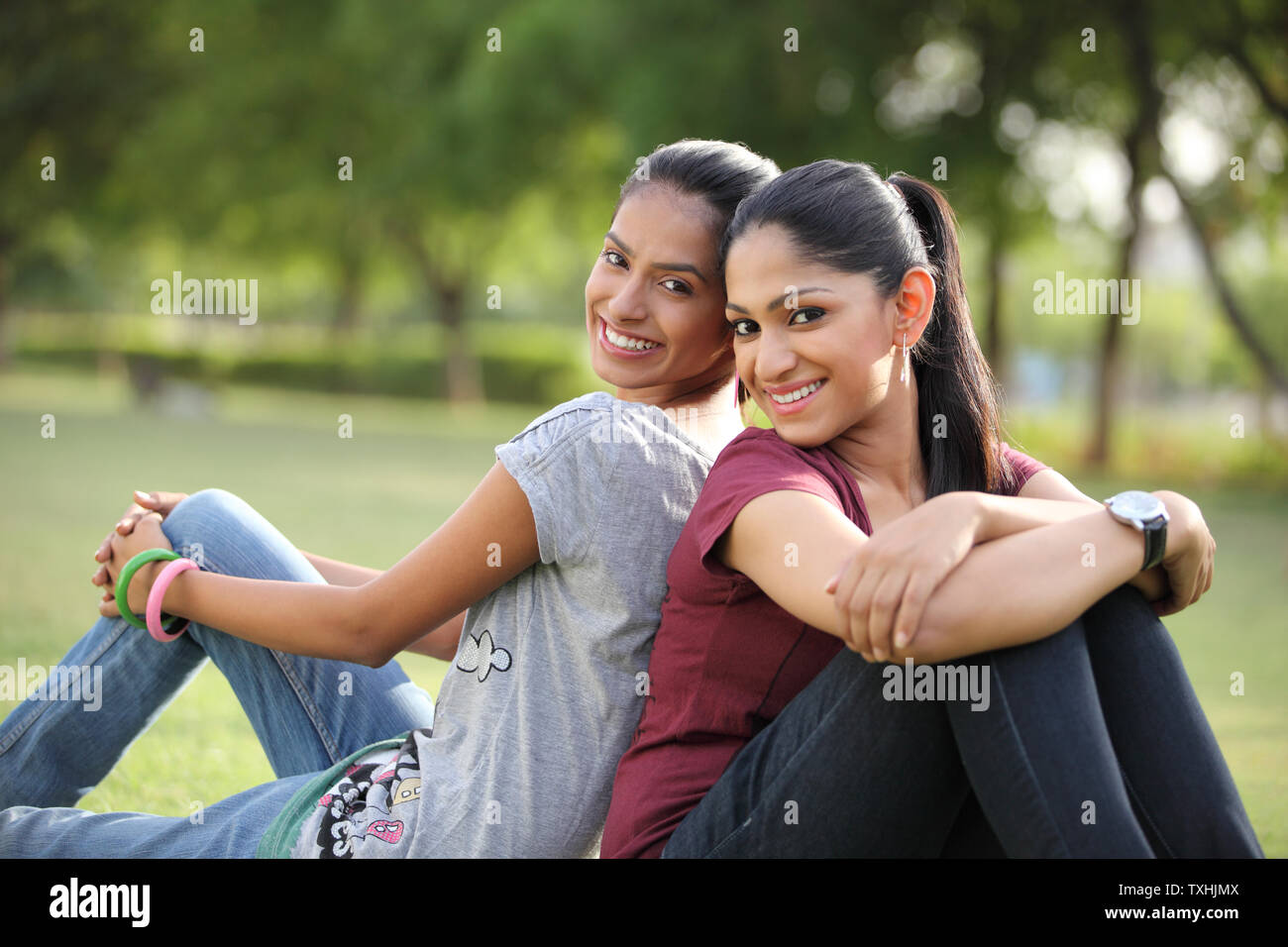 Portrait of two friends sitting back to back and smiling Stock Photo ...