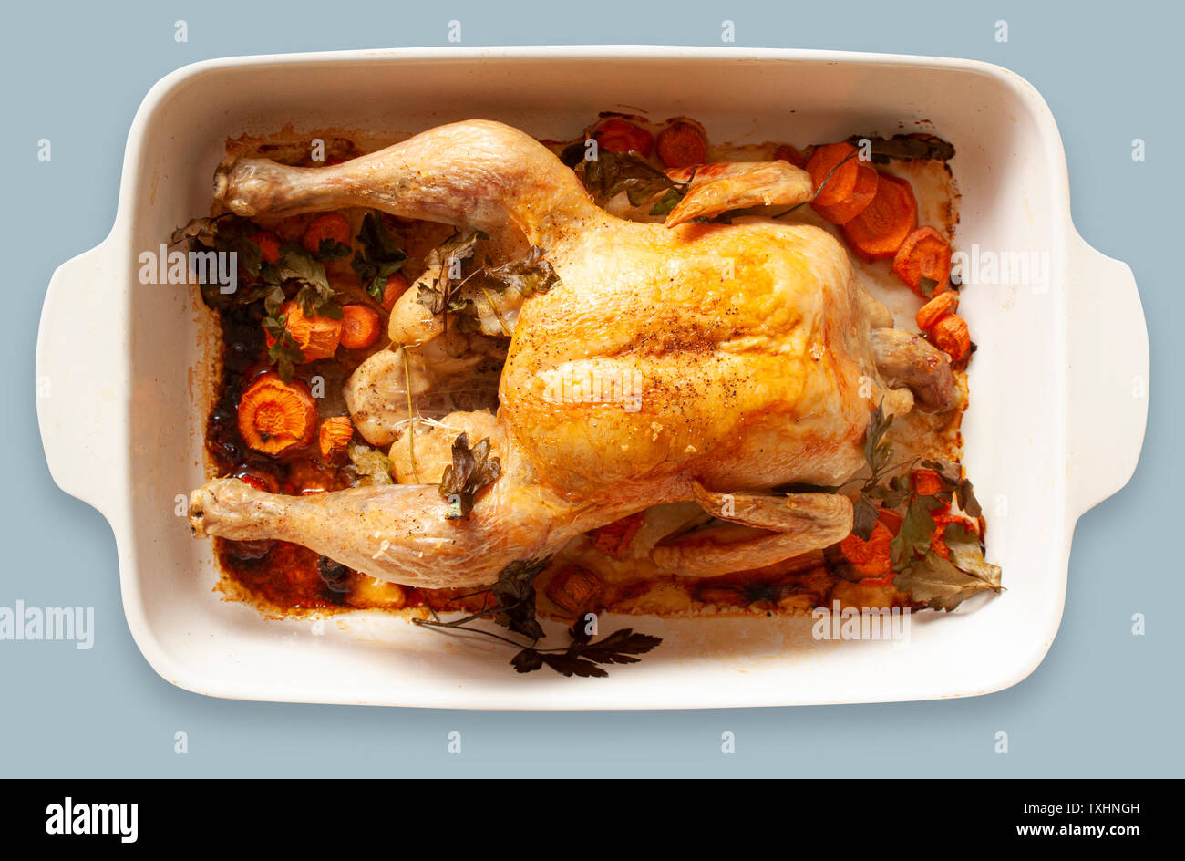 Oven-roasted chicken with vegetables in a baking dish. Top view image on light blue gray background. Stock Photo