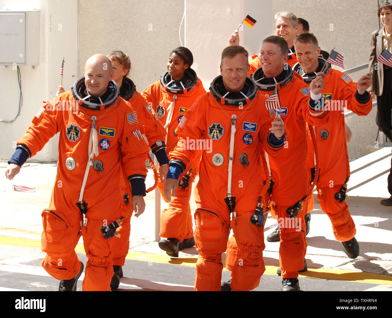 Commander Steven Lindsey (R) and Pilot Mark Kelly (L) wave American Flags as they lead Mission Specialists  Lisa Nowak (2nd Row,L), Michael Fossum (2nd row,R), Stephanie Wilson (3rd Row,L), Piers Sellers, (3rd Row,R), and Thomas Reiter (rear) of Germany, out of the Operations and Checkout Building to board the NASA Astrovan to board the Space Shuttle Discovery for mission STS-121 at Cape Canaveral, Florida on July 4, 2006.  Reiter is waving a German flag for the 4th of July launch. (UPI Photo/Pat Benic) Stock Photo