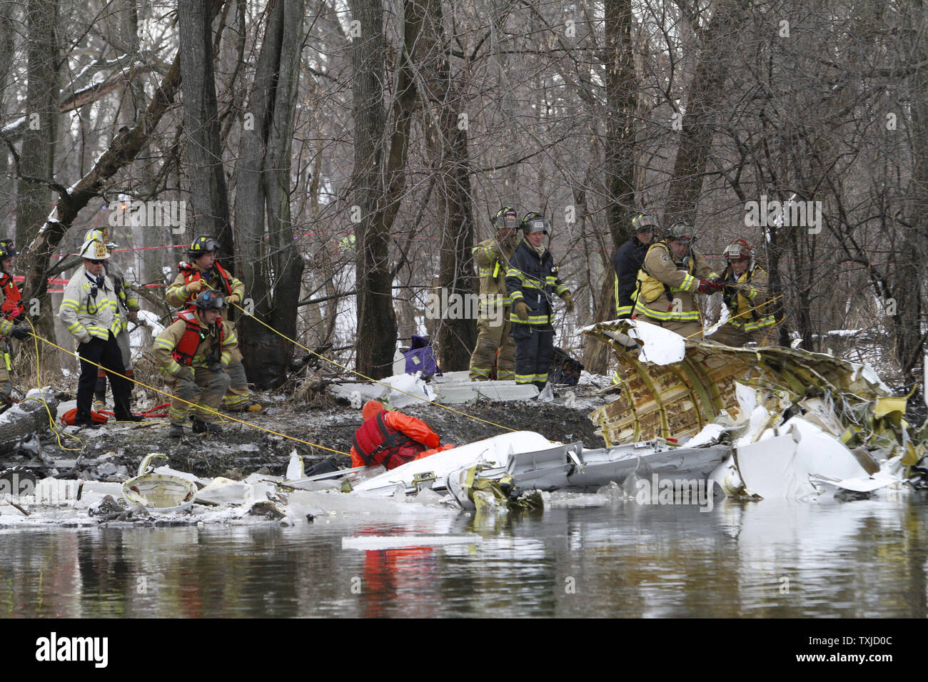 First responders use ropes to pull the wreckage of a small jet that
