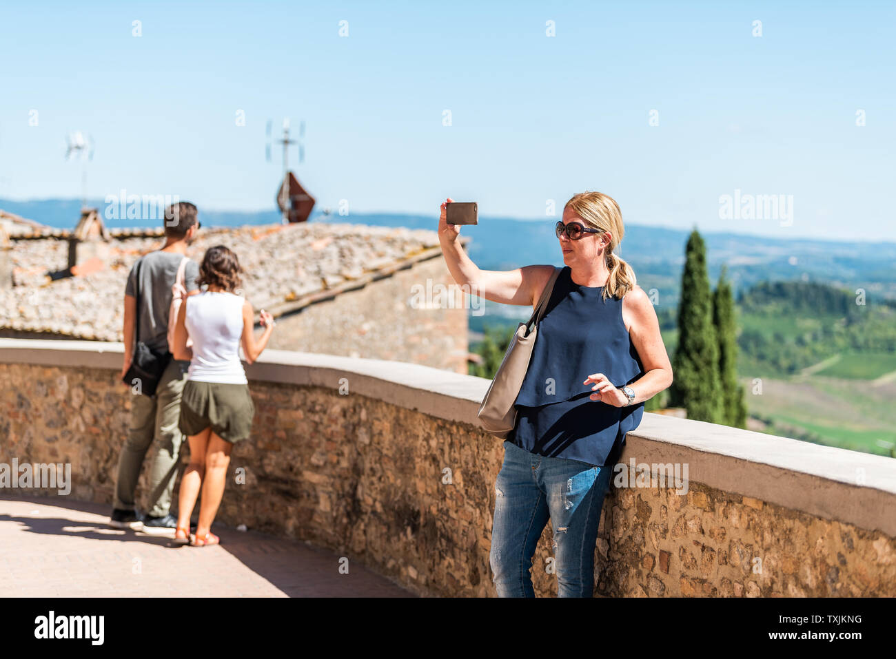 San Gimignano, Italy - August 27, 2018: People woman taking selfie picture exploring small historic medieval town village in Tuscany with view of roll Stock Photo
