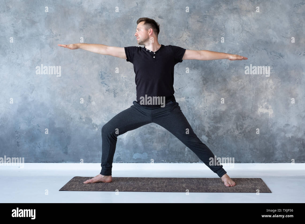 Man practicing yoga in studio doing Warrior 2 pose Stock Photo