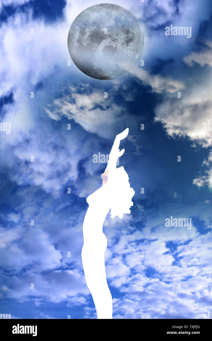 attractive silhouetted nude woman holding her hands up to the sky giving gratitude to the moon in a yoga pose with a cloudy background Stock Photo