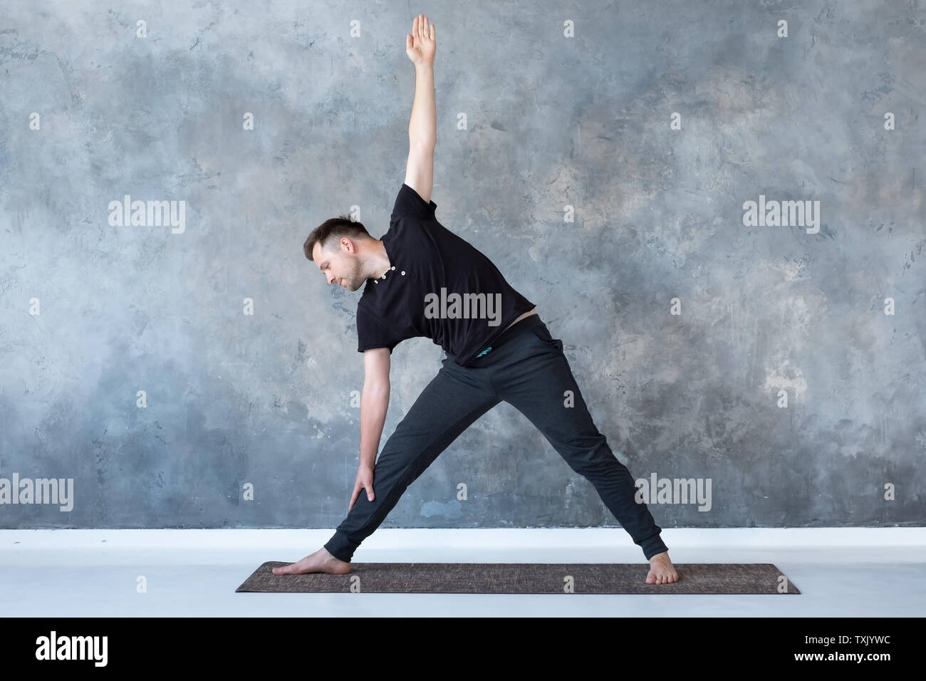 Man beginner practicing yoga doing trikonasana pose. Stock Photo