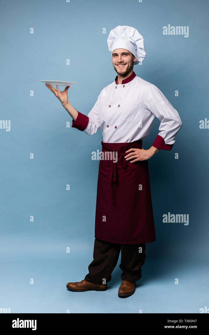 Happy male chef cook standing with plate isolated on light blue background. Stock Photo