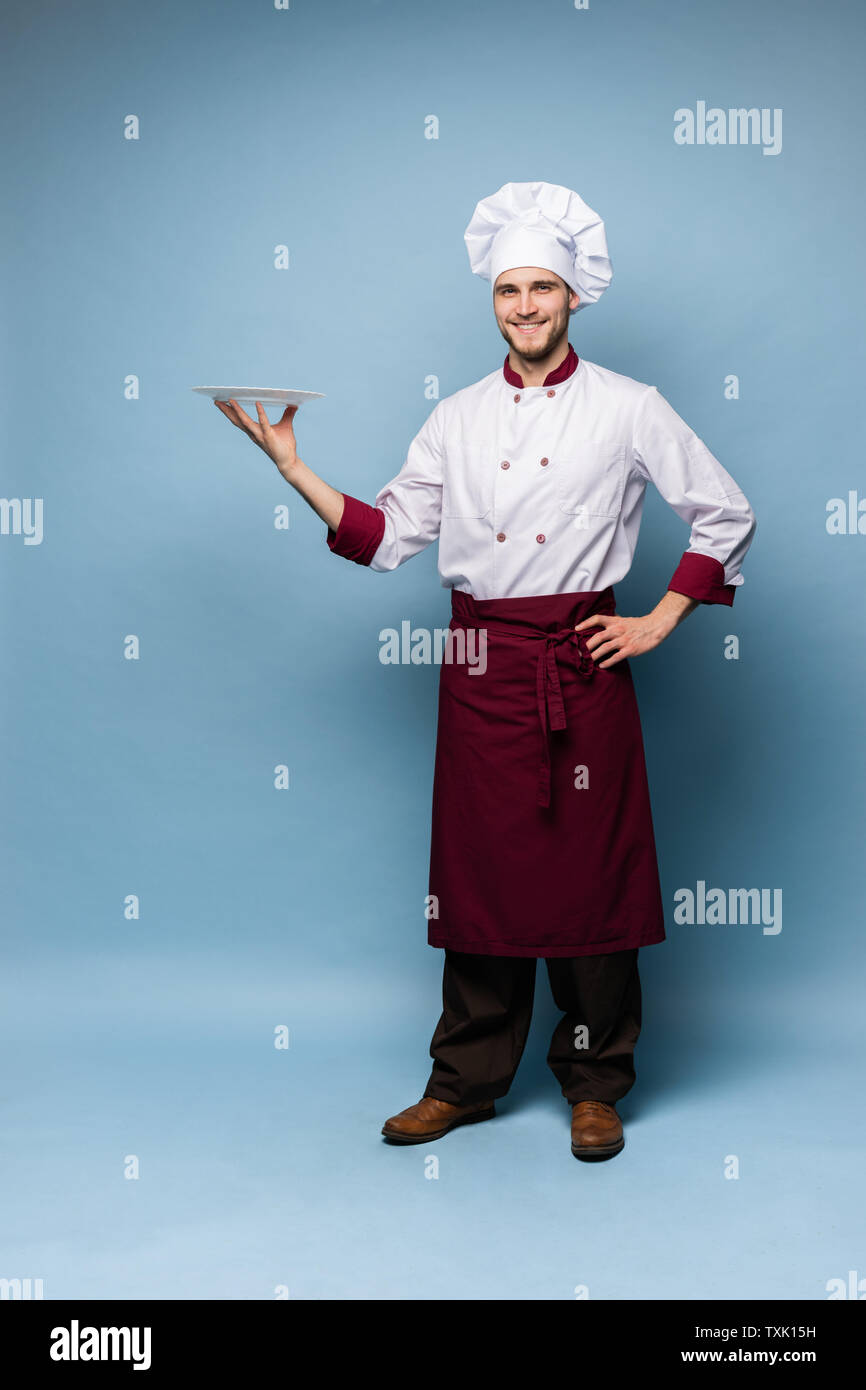 Happy male chef cook standing with plate isolated on light blue background. Stock Photo