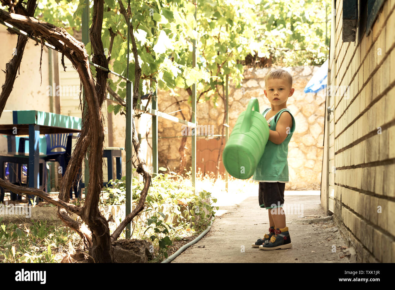 A little boy with a big green watering can is in the yard. Great mother's helper Stock Photo