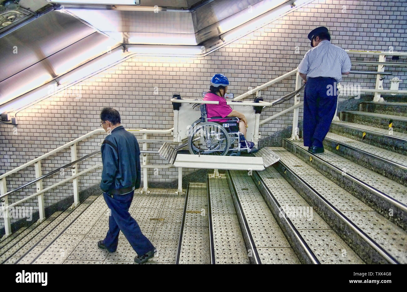 Subway staff officer helping a disable person on wheelchair to go up the stairs with a chairlift , Tokyo underground, Japan. Stock Photo