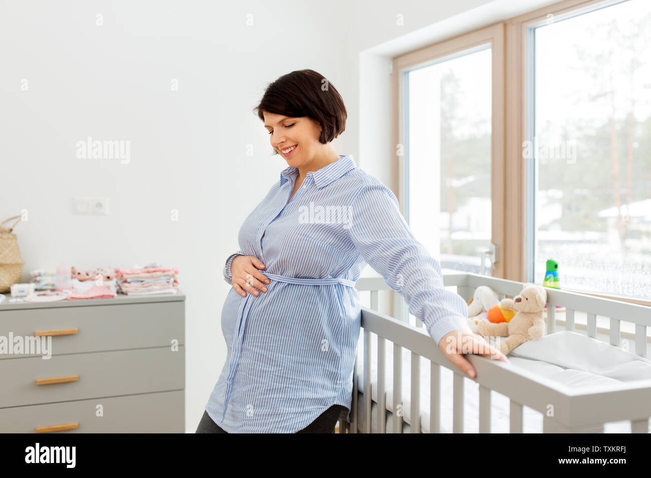 happy pregnant woman next to baby bed at home Stock Photo
