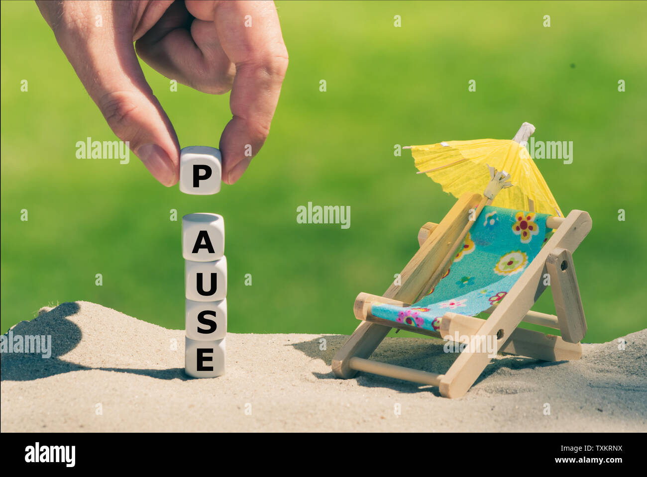 Concept for the summer break. Dice form the German word 'Pause' ('break' in English) next to a beach chair and a parasol. Stock Photo