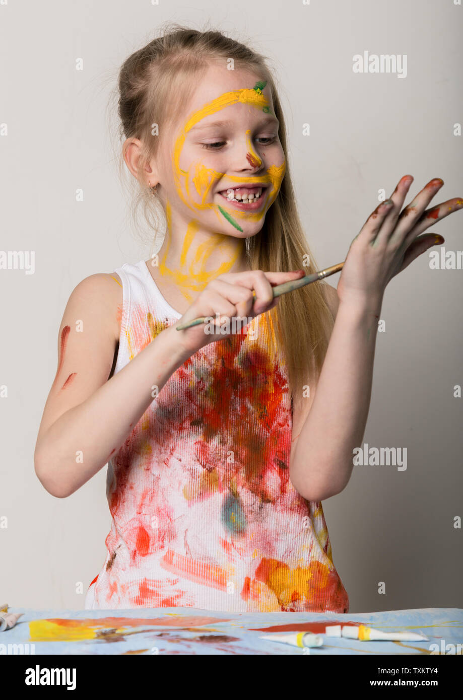 Cute little girl painter draws on the table and on himself on her ...
