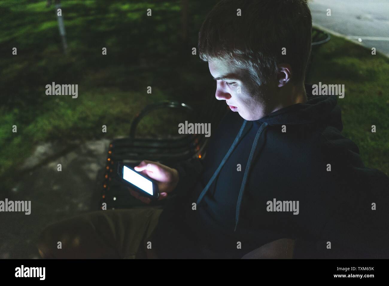 Depressed Teenager On His Cellphone While Sitting On A Park Bench