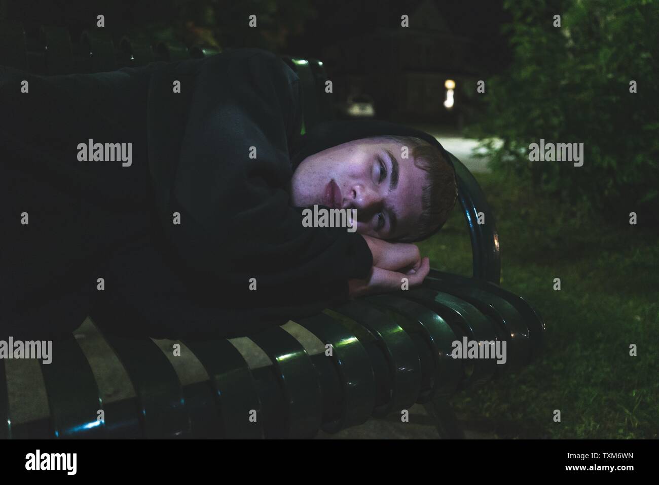 Homeless teen lying down on a park bench Stock Photo - Alamy