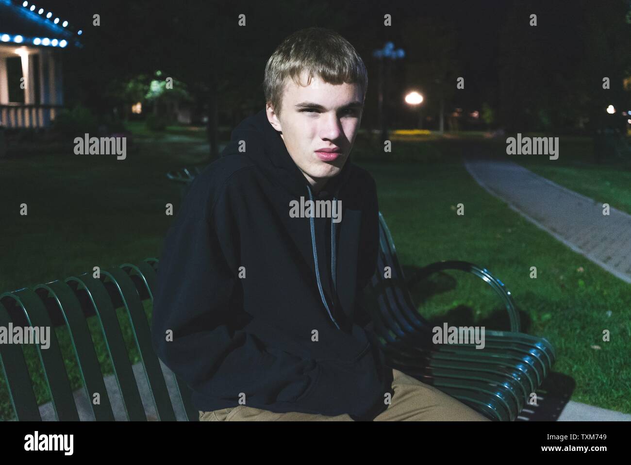 Sad teenage boy sitting on a park bench all alone at night Stock Photo ...