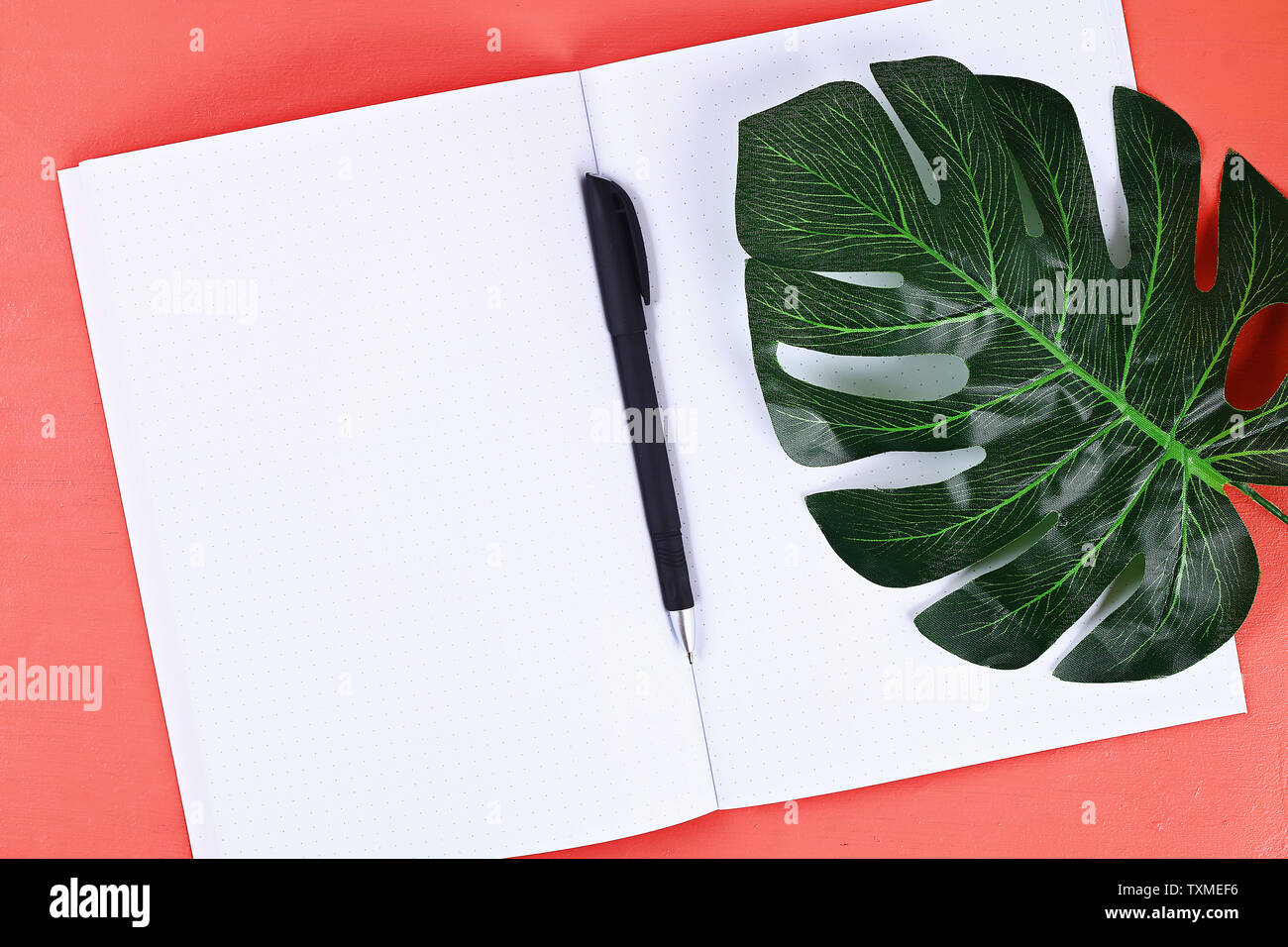 Blank notebook on coral background, tropical leaf. Top view, flat lay. Mockup, copy space. Summer background, travel. Stock Photo
