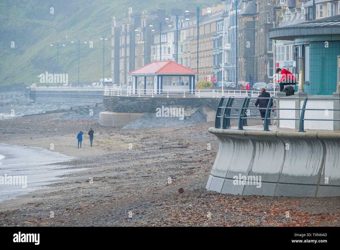 Aberystwyth Wales UK, Tuesday 25 June 2019 UK Weather: People at the seaside in Aberystwyth, wrapped up against the drizzle and rain on a dull damp and overcast afternoon . The conditions ares set to dramatically change be the weekend., with a plume of hot and sunny weather reaching up from the continent, bring ing temperatures in the mid 20's celsius photo Credit: keith morris/Alamy Live News Stock Photo
