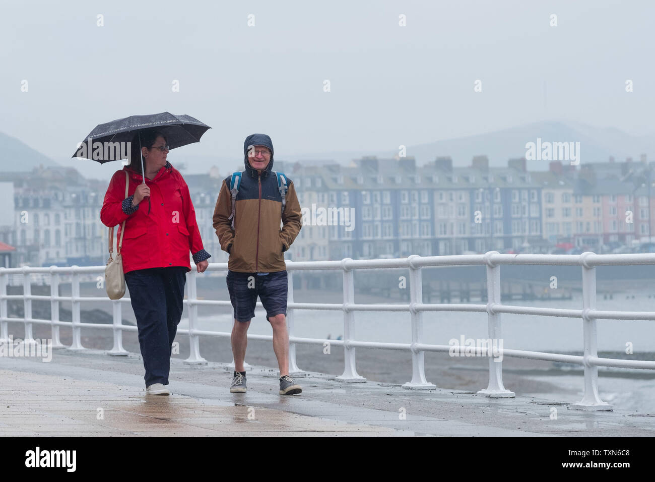 Aberystwyth Wales UK, Tuesday 25 June 2019 UK Weather: People walking on the promenade in Aberystwyth, wrapped up against the drizzle and and holding umbrellas against the rain on a dull damp and overcast afternoon . The conditions ares set to dramatically change be the weekend., with a plume of hot and sunny weather reaching up from the continent, bring ing temperatures in the mid 20's celsius photo Credit: keith morris/Alamy Live News Stock Photo