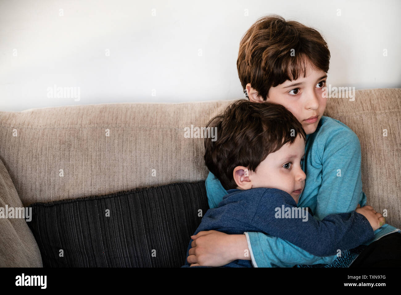 Big brother hugging toddler, staring in disbelief on sofa Stock Photo