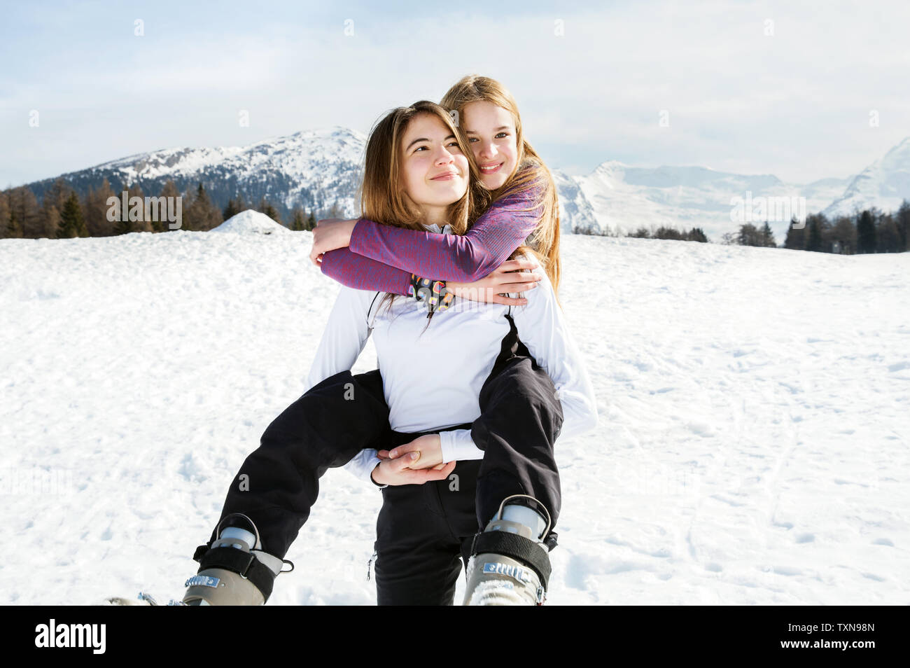 Teenage girl skier getting piggyback from best friend in snow covered landscape, portrait, Tyrol, Styria, Austria Stock Photo